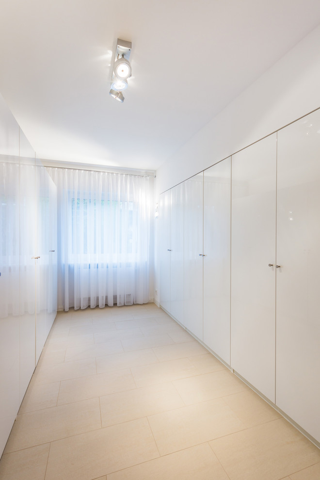 This is an example of a mid-sized contemporary built-in wardrobe in Frankfurt with flat-panel cabinets, white cabinets, ceramic floors and beige floor.
