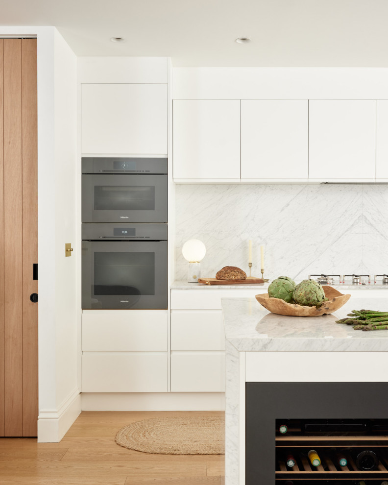 Diseño de cocina actual con fregadero de doble seno, puertas de armario blancas, electrodomésticos negros, suelo de madera clara, una isla y suelo marrón