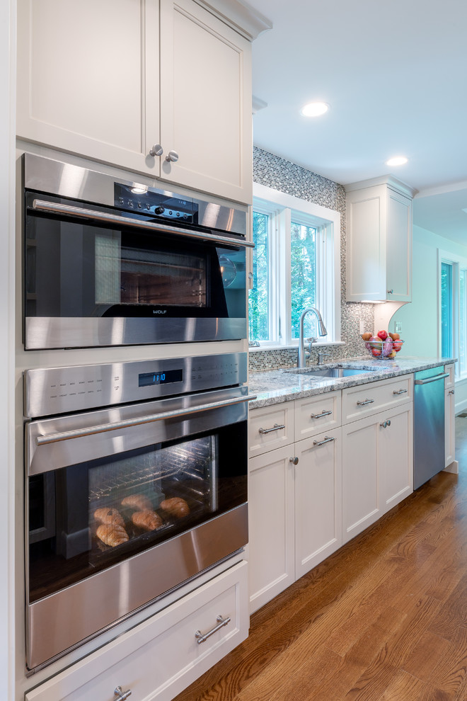Kitchen - kitchen idea in Boston with white cabinets, mosaic tile backsplash, stainless steel appliances and an island