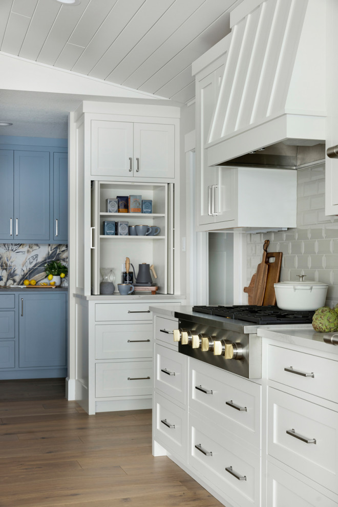 This is an example of a large beach style l-shaped eat-in kitchen in Minneapolis with an undermount sink, shaker cabinets, white cabinets, quartz benchtops, grey splashback, subway tile splashback, panelled appliances, with island, white benchtop, light hardwood floors, brown floor and vaulted.
