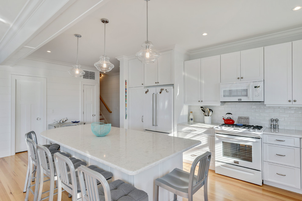 Beach style l-shaped eat-in kitchen in New York with a farmhouse sink, recessed-panel cabinets, white cabinets, marble benchtops, white splashback, ceramic splashback, stainless steel appliances, light hardwood floors and with island.