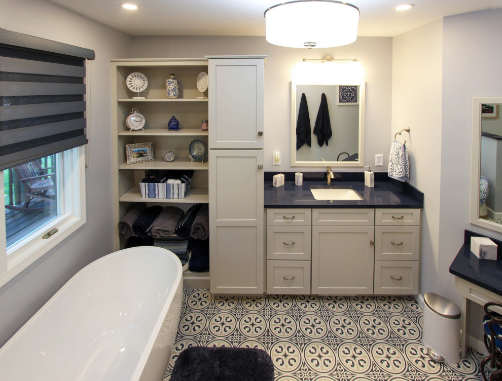 Mid-sized transitional master gray tile and subway tile limestone floor and blue floor freestanding bathtub photo in Cleveland with flat-panel cabinets, gray cabinets, a two-piece toilet, gray walls, an undermount sink, quartz countertops, a hinged shower door and blue countertops