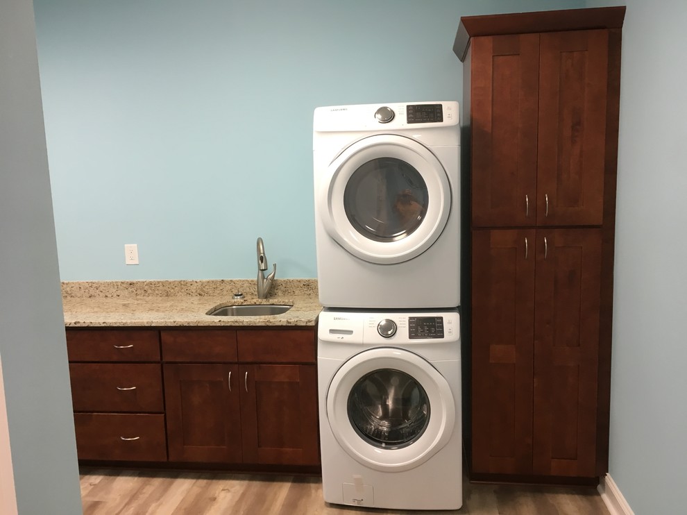 Large country l-shaped utility room in Other with an undermount sink, flat-panel cabinets, medium wood cabinets, granite benchtops, blue walls, vinyl floors, a stacked washer and dryer and beige floor.