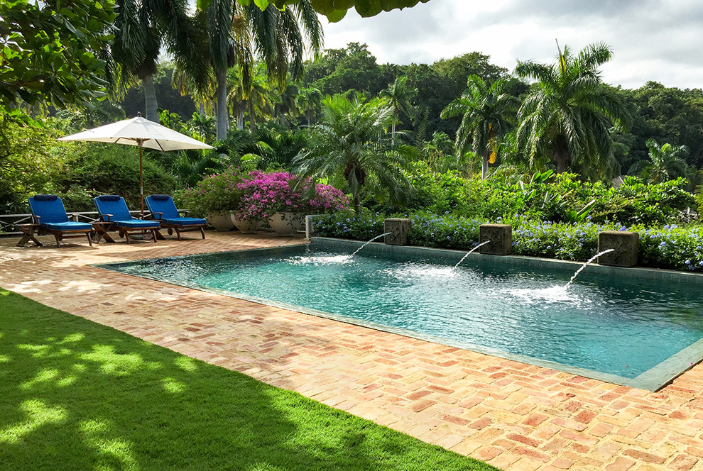 Tropical rectangular pool in Miami with a water feature and brick pavers.