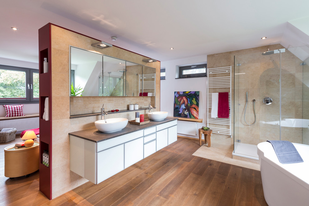 Photo of an expansive contemporary master wet room bathroom in Dusseldorf with flat-panel cabinets, white cabinets, a freestanding tub, beige tile, porcelain tile, white walls, medium hardwood floors, a vessel sink, brown floor and a hinged shower door.