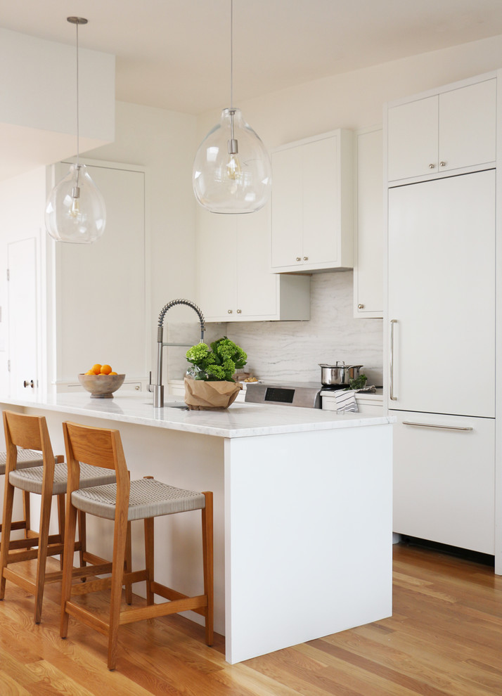 Design ideas for a contemporary galley kitchen in Boston with an undermount sink, flat-panel cabinets, white cabinets, white splashback, panelled appliances, medium hardwood floors, with island and brown floor.