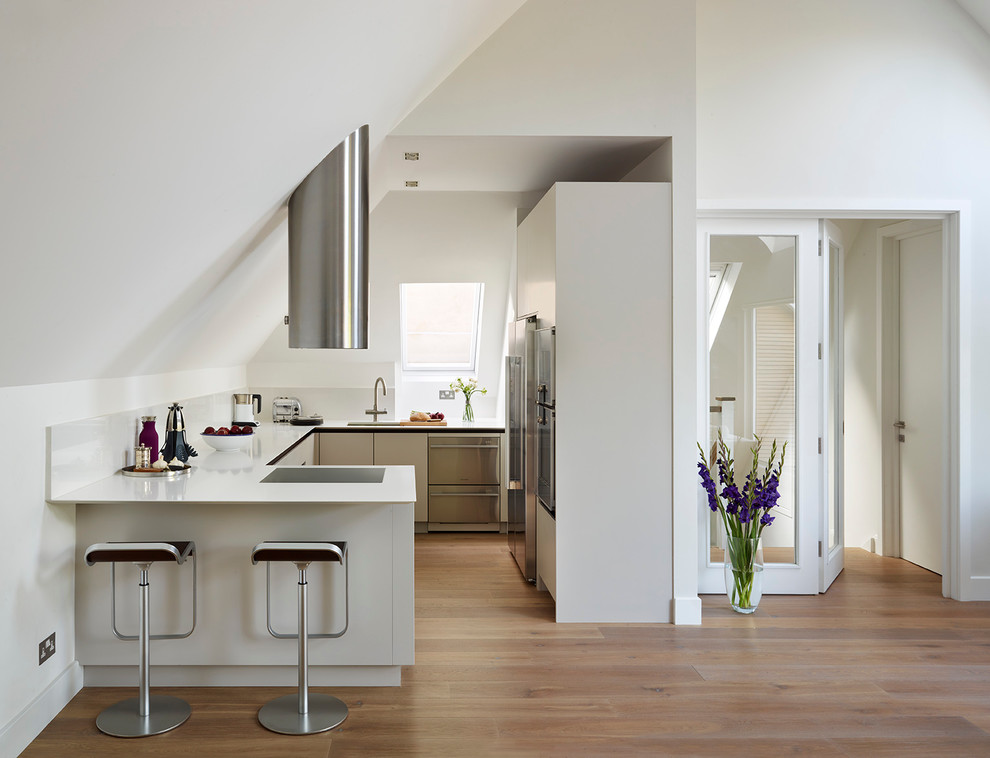 Design ideas for a small contemporary open plan kitchen in London with an undermount sink, flat-panel cabinets, white cabinets, solid surface benchtops and stainless steel appliances.
