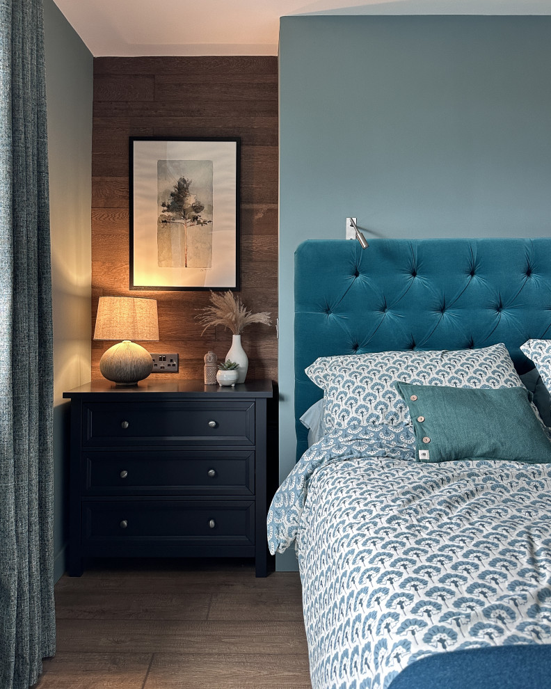 Ejemplo de dormitorio principal tradicional de tamaño medio con paredes azules, suelo laminado, suelo marrón y panelado