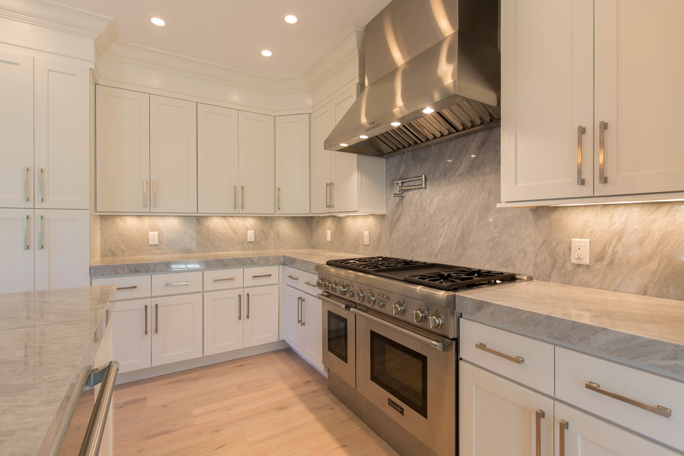 Example of a mid-sized transitional l-shaped light wood floor eat-in kitchen design in Miami with an undermount sink, recessed-panel cabinets, marble countertops, stainless steel appliances, an island, white cabinets, gray backsplash and stone slab backsplash