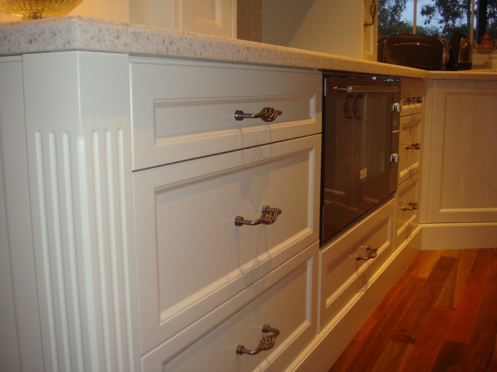 Photo of a mid-sized traditional l-shaped eat-in kitchen in Newcastle - Maitland with recessed-panel cabinets, white cabinets, quartz benchtops, white splashback, with island and white benchtop.