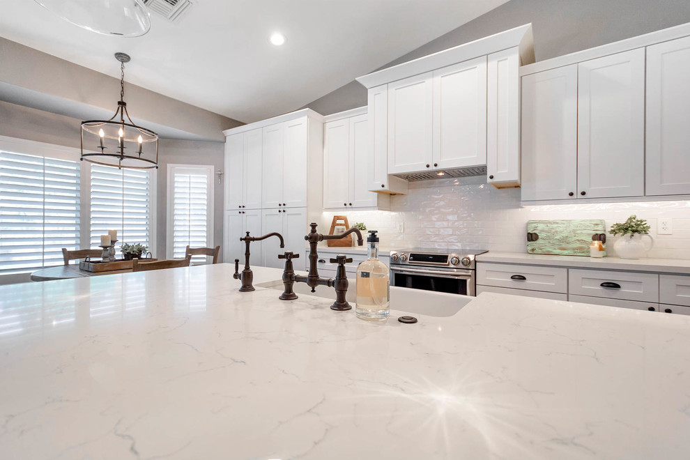 Inspiration for a large country l-shaped open plan kitchen in Phoenix with a farmhouse sink, shaker cabinets, white cabinets, quartz benchtops, white splashback, subway tile splashback, stainless steel appliances, with island and white benchtop.