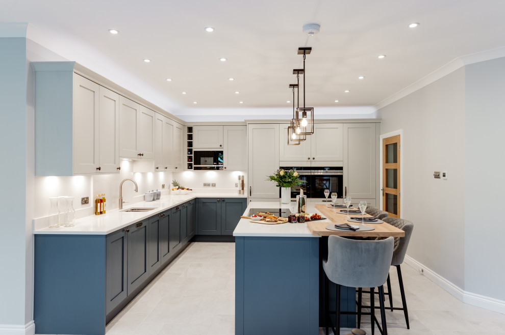 Large traditional l-shaped open plan kitchen in Surrey with an integrated sink, shaker cabinets, blue cabinets, quartzite benchtops, white splashback, engineered quartz splashback, panelled appliances, porcelain floors, with island, grey floor and white benchtop.