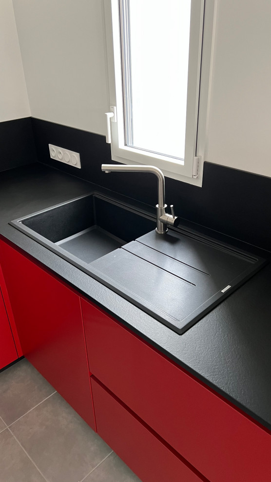 Foto på ett litet funkis svart kök, med en undermonterad diskho, röda skåp, laminatbänkskiva, svart stänkskydd, integrerade vitvaror och grått golv