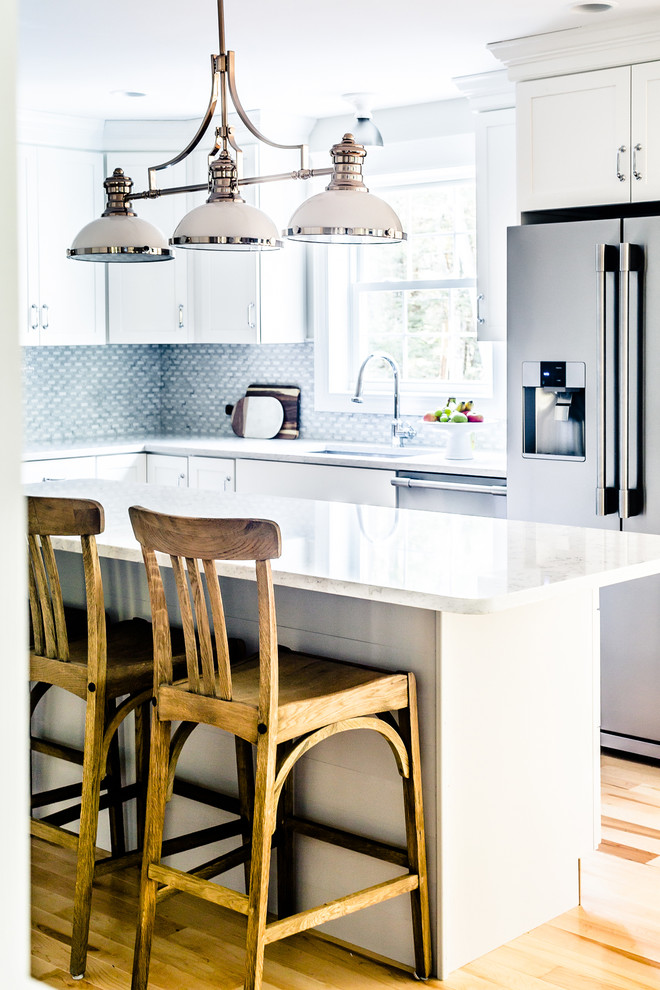 Transitional kitchen in Portland Maine with an undermount sink, shaker cabinets, white cabinets, grey splashback, stainless steel appliances, light hardwood floors and with island.