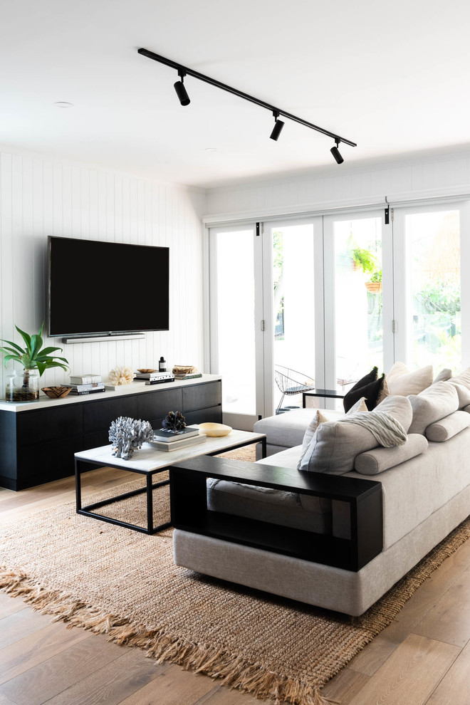 This is an example of a beach style living room with white walls, medium hardwood floors, a wall-mounted tv and brown floor.