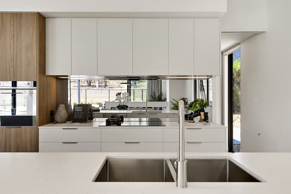 Mid-sized contemporary single-wall eat-in kitchen in Canberra - Queanbeyan with an undermount sink, flat-panel cabinets, white cabinets, quartz benchtops, metallic splashback, mirror splashback, black appliances, concrete floors, with island, grey floor and white benchtop.