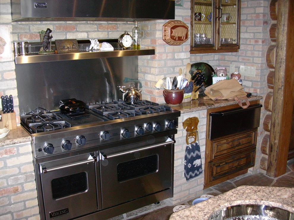 Esempio di una grande cucina ad U rustica con ante con bugna sagomata, ante con finitura invecchiata, top in granito, paraspruzzi in mattoni, elettrodomestici in acciaio inossidabile e 2 o più isole