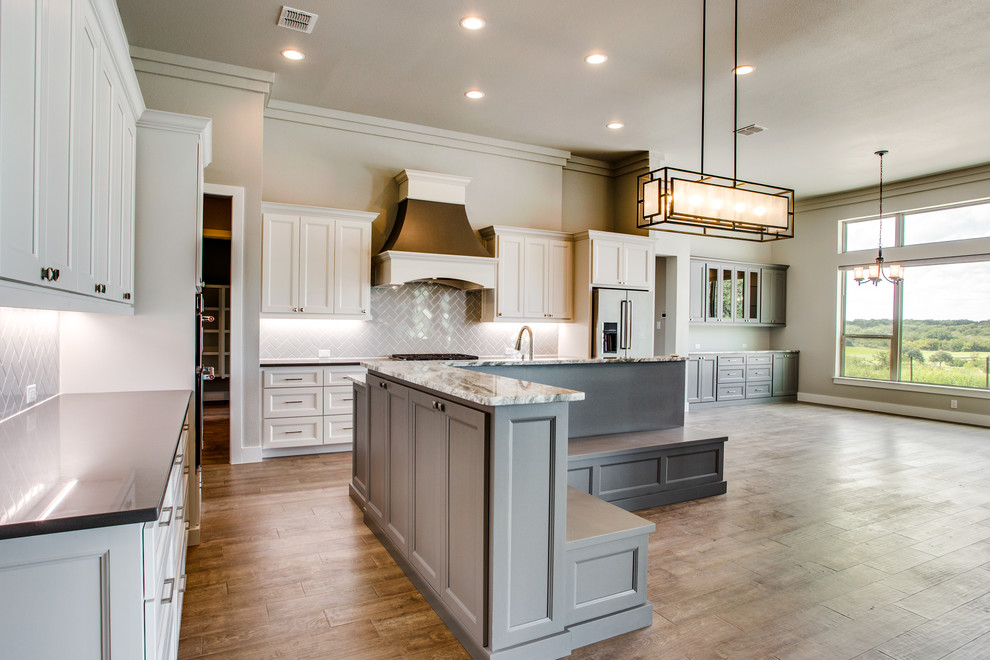 Open concept kitchen - transitional l-shaped medium tone wood floor and brown floor open concept kitchen idea in Austin with recessed-panel cabinets, white cabinets, gray backsplash, ceramic backsplash, stainless steel appliances, an island and gray countertops