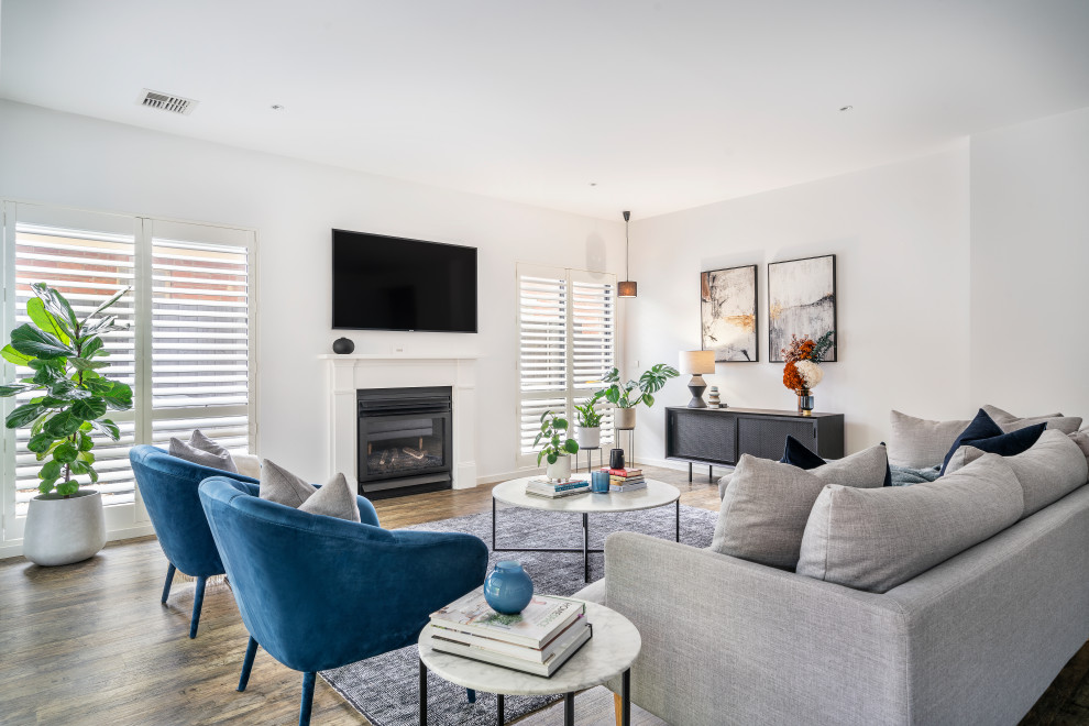 This is an example of a mid-sized contemporary open concept living room in Melbourne with white walls, laminate floors, a standard fireplace, a wood fireplace surround, a wall-mounted tv, brown floor, recessed and panelled walls.