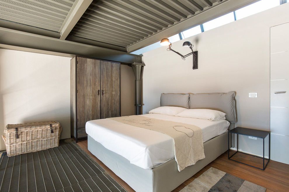 This is an example of a small industrial loft-style bedroom in Milan with beige walls, medium hardwood floors and multi-coloured floor.