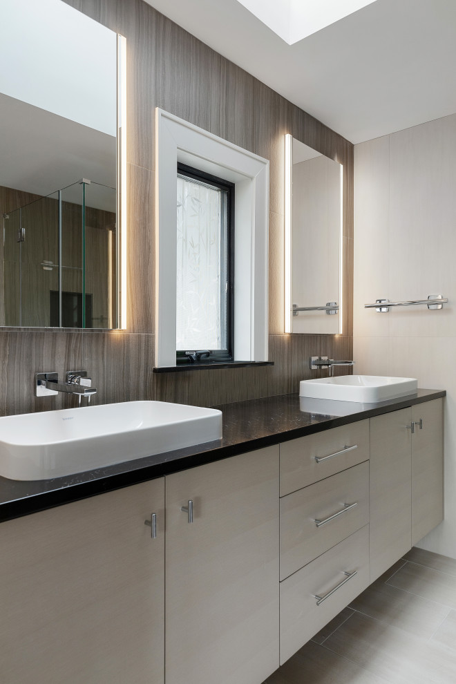 Photo of a large transitional master bathroom in New York with flat-panel cabinets, beige cabinets, a corner shower, a wall-mount toilet, brown tile, ceramic tile, grey walls, ceramic floors, a vessel sink, engineered quartz benchtops, grey floor, a hinged shower door, black benchtops, a double vanity and a built-in vanity.