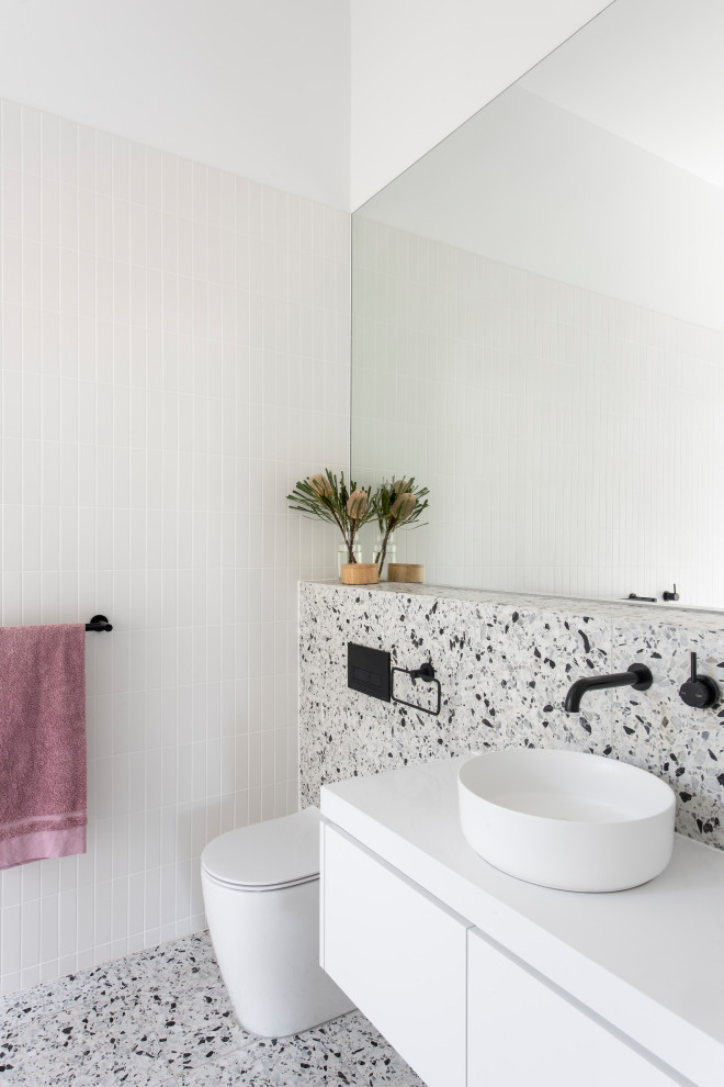 This is an example of a mid-sized contemporary master bathroom in Adelaide with recessed-panel cabinets, white cabinets, a freestanding tub, an open shower, white tile, ceramic tile, white walls, terrazzo floors, solid surface benchtops, white floor, an open shower, white benchtops, an enclosed toilet, a single vanity, a floating vanity and wood walls.