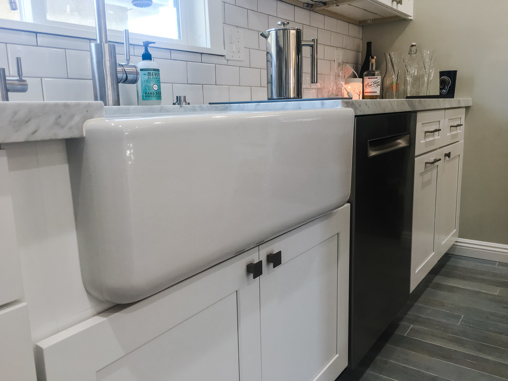 Large country u-shaped eat-in kitchen in Los Angeles with a farmhouse sink, recessed-panel cabinets, white cabinets, marble benchtops, white splashback, subway tile splashback, stainless steel appliances, porcelain floors, with island, grey floor and white benchtop.