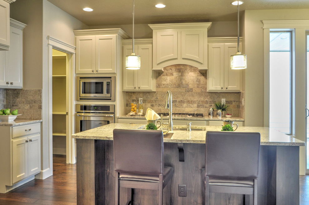 Small transitional l-shaped medium tone wood floor eat-in kitchen photo in Boise with an undermount sink, recessed-panel cabinets, white cabinets, granite countertops, beige backsplash, stone tile backsplash, stainless steel appliances and an island