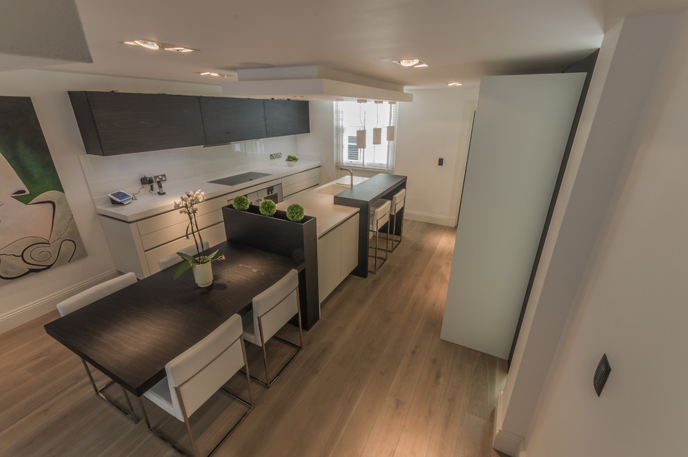 This is an example of a contemporary galley open plan kitchen in Cheshire with dark wood cabinets, granite benchtops, stainless steel appliances, light hardwood floors and with island.