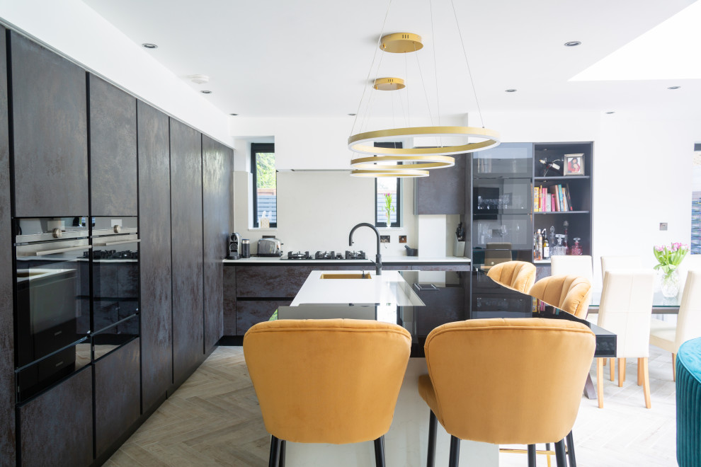 Mittelgroße Moderne Wohnküche in L-Form mit Waschbecken, flächenbündigen Schrankfronten, Glas-Arbeitsplatte, Elektrogeräten mit Frontblende, Kücheninsel und schwarzer Arbeitsplatte in Essex