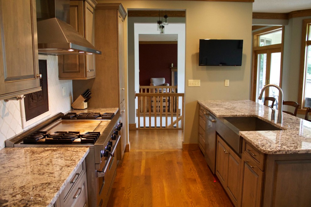 Inspiration for a mid-sized transitional galley medium tone wood floor eat-in kitchen remodel with a farmhouse sink, recessed-panel cabinets, gray cabinets, granite countertops, white backsplash, ceramic backsplash, stainless steel appliances and a peninsula
