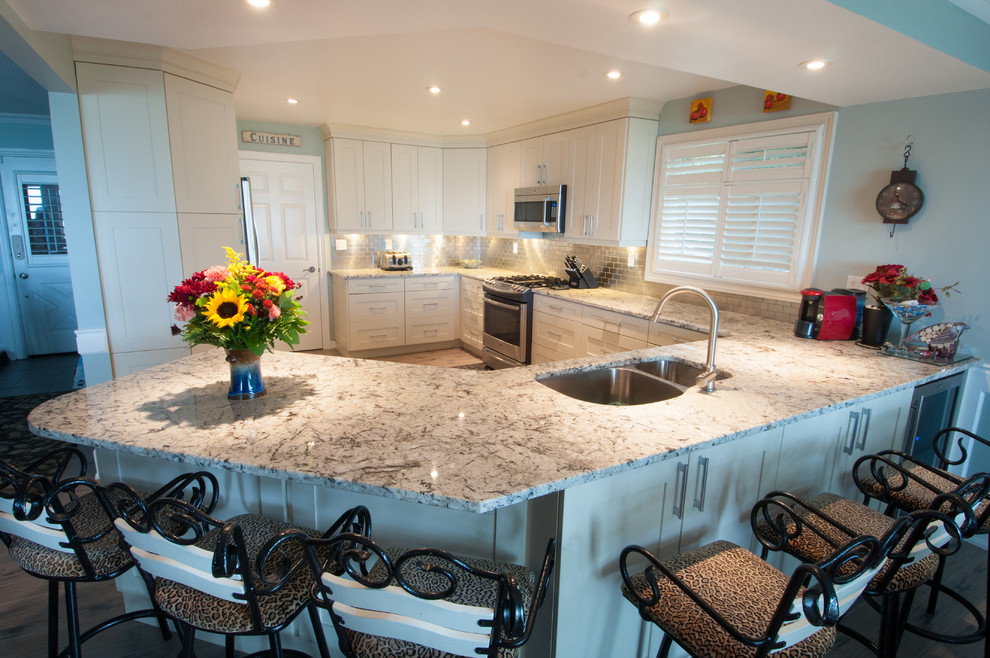 Mid-sized transitional light wood floor and brown floor enclosed kitchen photo in Toronto with a double-bowl sink, shaker cabinets, white cabinets, marble countertops, metallic backsplash, subway tile backsplash, stainless steel appliances and a peninsula