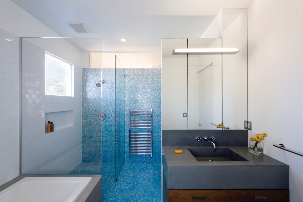 Mid-sized modern 3/4 bathroom in New York with flat-panel cabinets, dark wood cabinets, a drop-in tub, a curbless shower, blue tile, glass tile, porcelain floors, an integrated sink, concrete benchtops and a one-piece toilet.