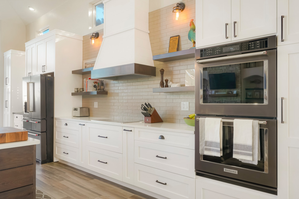 Open concept kitchen - large transitional single-wall vaulted ceiling open concept kitchen idea in Denver with a farmhouse sink, shaker cabinets, white cabinets, white backsplash, subway tile backsplash, black appliances, an island and white countertops