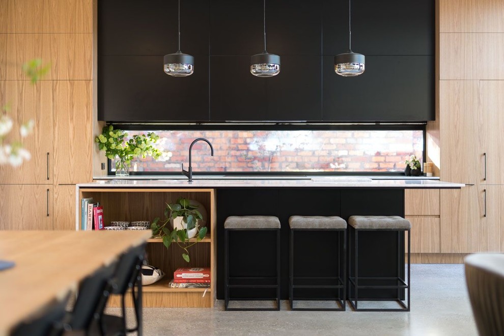 Modern galley open plan kitchen in Melbourne with a drop-in sink, recessed-panel cabinets, black cabinets, quartz benchtops, glass sheet splashback, black appliances, concrete floors and with island.