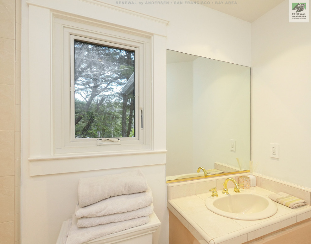 Пример оригинального дизайна: ванная комната среднего размера с светлыми деревянными фасадами, ванной в нише, душем над ванной, раздельным унитазом, бежевой плиткой, керамической плиткой, белыми стенами, полом из керамической плитки, накладной раковиной, столешницей из плитки, белым полом, шторкой для ванной, бежевой столешницей, тумбой под одну раковину, встроенной тумбой и сводчатым потолком