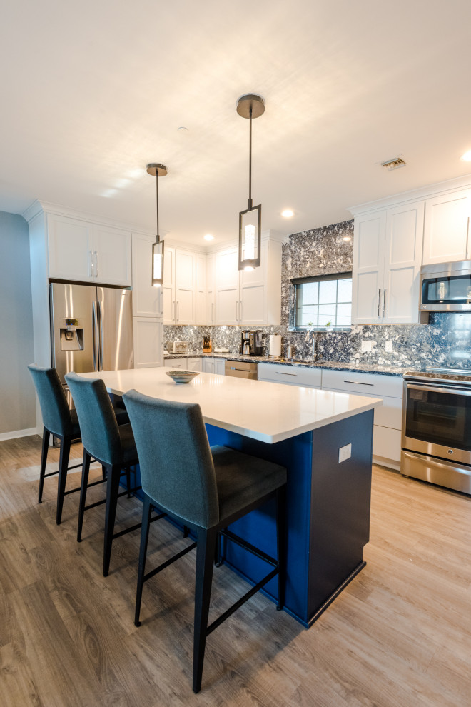 Photo of a mid-sized industrial l-shaped eat-in kitchen in Baltimore with an undermount sink, white cabinets, quartz benchtops, blue splashback, engineered quartz splashback, stainless steel appliances, vinyl floors, brown floor and blue benchtop.