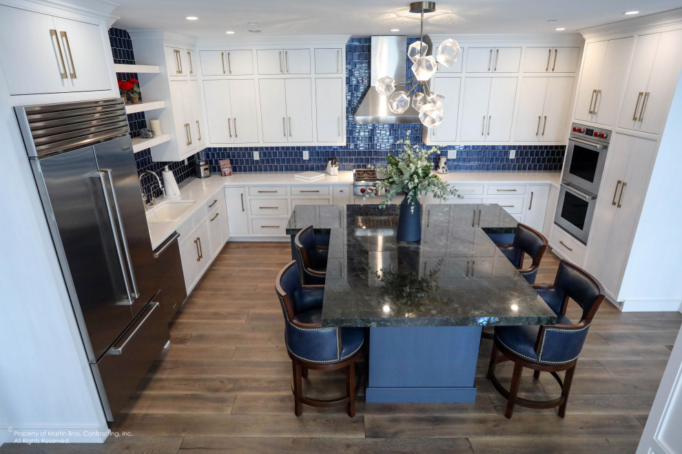 Inspiration for a large transitional u-shaped medium tone wood floor open concept kitchen remodel with a single-bowl sink, flat-panel cabinets, white cabinets, quartz countertops, blue backsplash, glass tile backsplash, stainless steel appliances, an island and white countertops