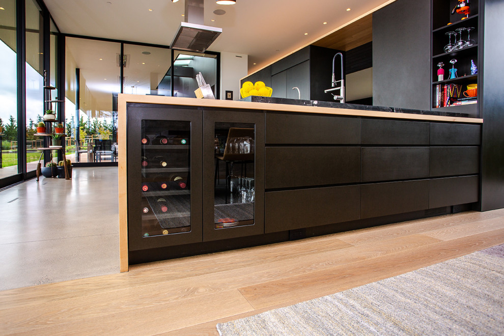 Inspiration for a modern l-shaped eat-in kitchen in Portland with flat-panel cabinets, black cabinets, wood benchtops, with island, a drop-in sink, panelled appliances, concrete floors, beige floor and black benchtop.