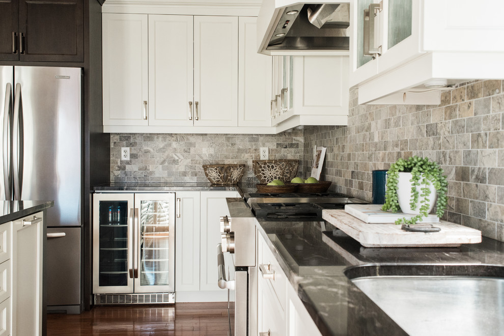 Design ideas for a transitional kitchen in Toronto with an undermount sink, recessed-panel cabinets, white cabinets, granite benchtops, grey splashback, travertine splashback, stainless steel appliances, medium hardwood floors, with island and brown floor.
