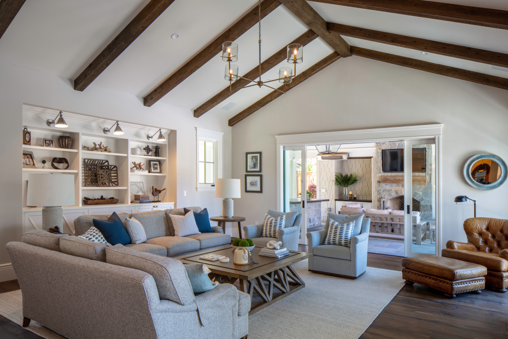 Design ideas for an expansive beach style open concept family room in San Francisco with beige walls, dark hardwood floors, a standard fireplace, a stone fireplace surround, a wall-mounted tv, brown floor and exposed beam.