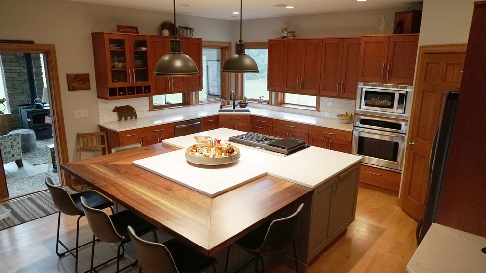 Large transitional l-shaped medium tone wood floor open concept kitchen photo with an undermount sink, recessed-panel cabinets, brown cabinets, white backsplash, subway tile backsplash, stainless steel appliances, an island and white countertops