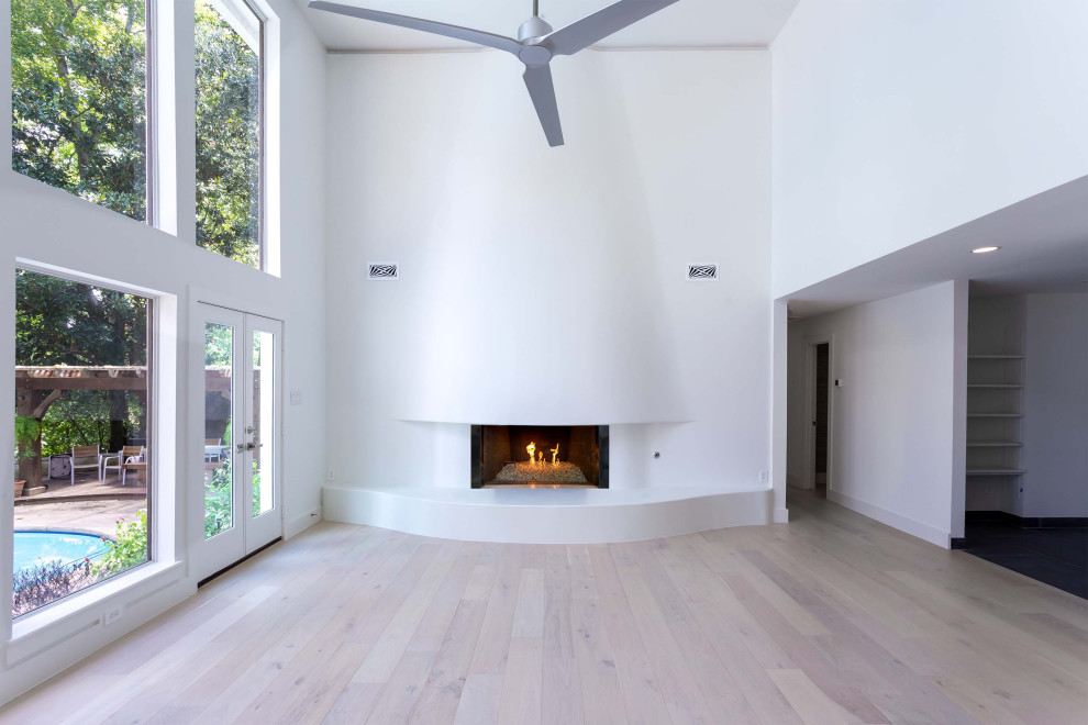 Inspiration for an expansive modern living room in Houston with medium hardwood flooring, a hanging fireplace, a plastered fireplace surround, white floors and wood walls.