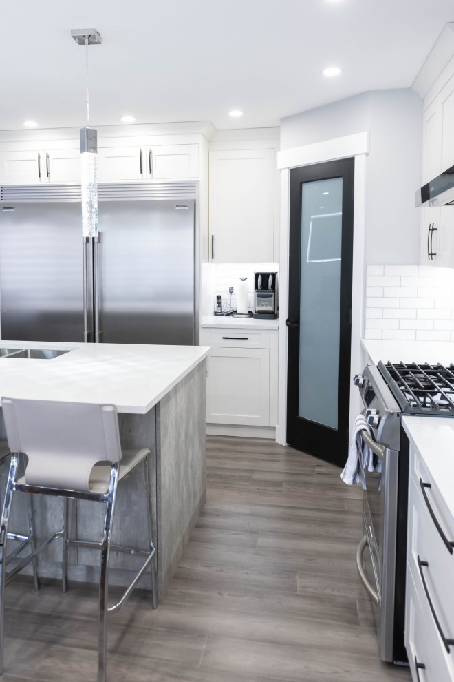 Mid-sized minimalist l-shaped light wood floor and gray floor eat-in kitchen photo in Calgary with an undermount sink, shaker cabinets, white cabinets, quartzite countertops, white backsplash, subway tile backsplash, stainless steel appliances, an island and white countertops