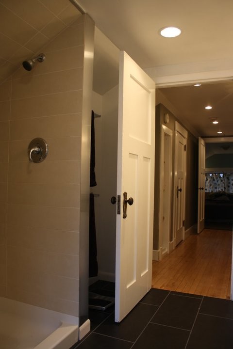 This is an example of a mid-sized contemporary 3/4 bathroom in Cedar Rapids with open cabinets, an alcove shower, beige tile, porcelain tile, white walls, linoleum floors, a vessel sink, glass benchtops, black floor and an open shower.