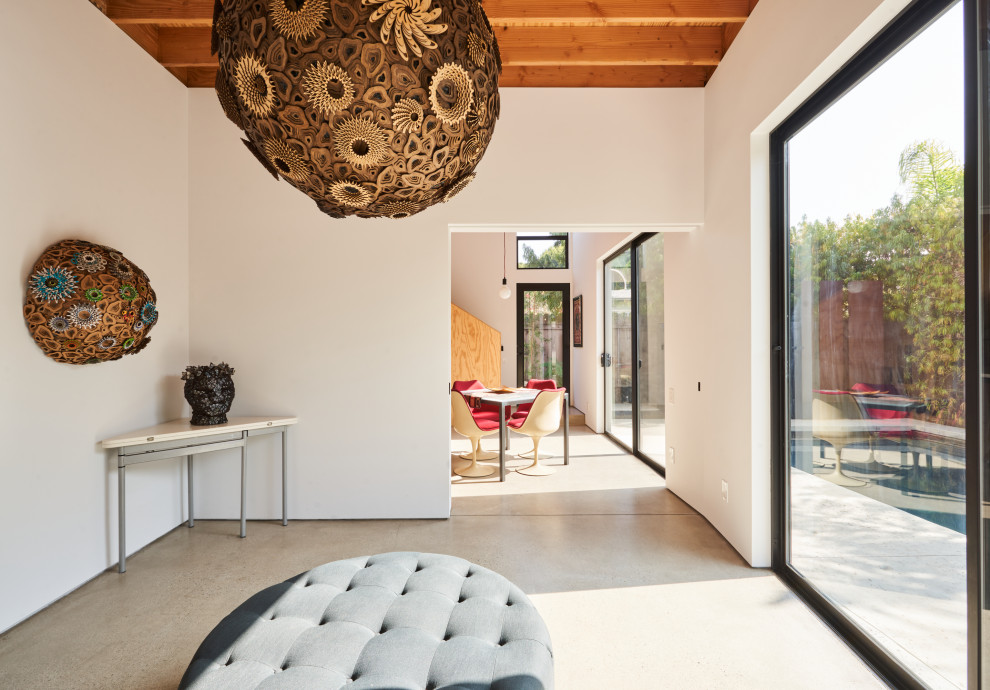 Cette image montre un petit salon nordique ouvert avec un mur blanc, sol en béton ciré, un sol gris et poutres apparentes.