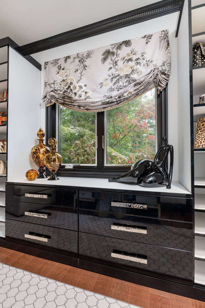 This is an example of a mid-sized transitional women's dressing room in New York with flat-panel cabinets, black cabinets, dark hardwood floors and brown floor.