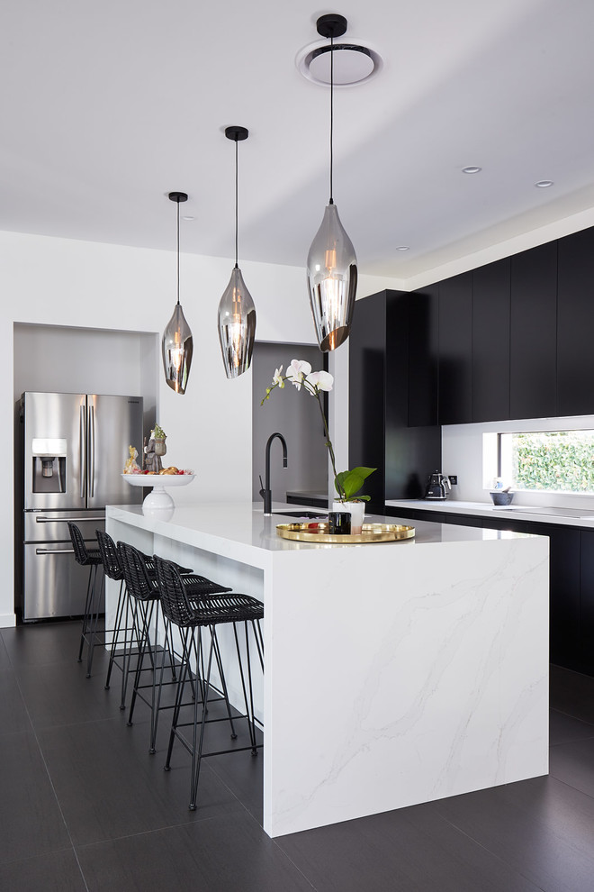Photo of a contemporary l-shaped kitchen in Sydney with an undermount sink, flat-panel cabinets, white splashback, stainless steel appliances, with island, black floor and white benchtop.