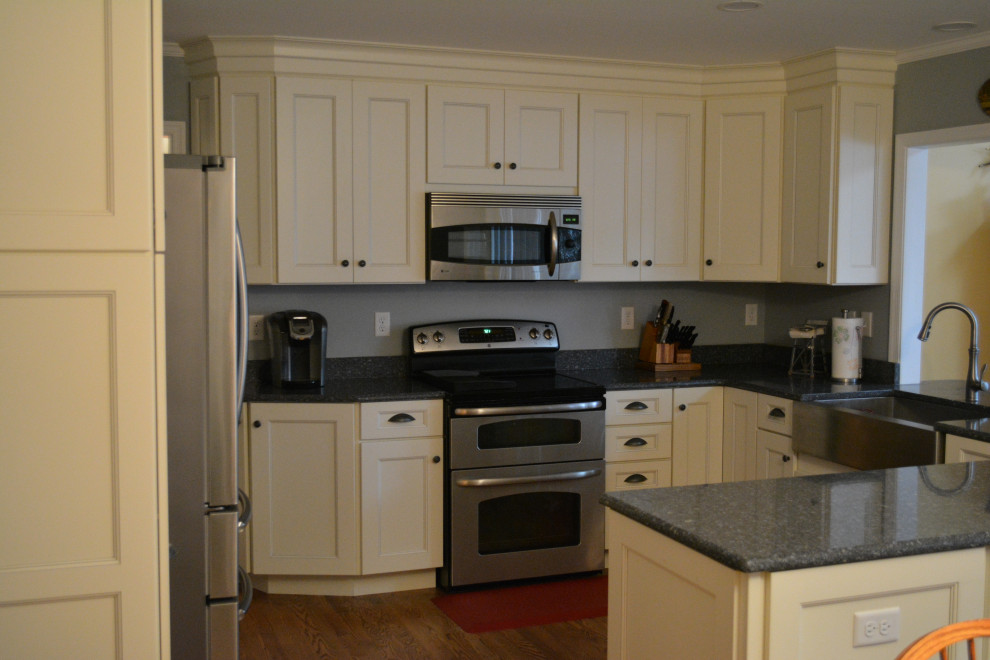 Example of a mid-sized transitional u-shaped dark wood floor and brown floor eat-in kitchen design with a farmhouse sink, shaker cabinets, beige cabinets, granite countertops, gray backsplash, mosaic tile backsplash, stainless steel appliances, a peninsula and black countertops