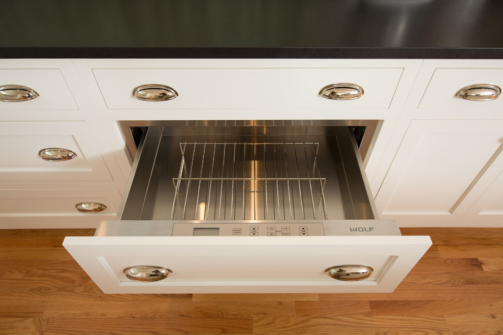 Example of a transitional medium tone wood floor home design design in Boston with a farmhouse sink, recessed-panel cabinets, white cabinets, granite countertops, white backsplash, subway tile backsplash, stainless steel appliances and two islands
